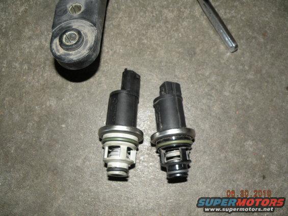 two automotive sensors with electrical connectors and internal springs, one is lighter in color than the other
