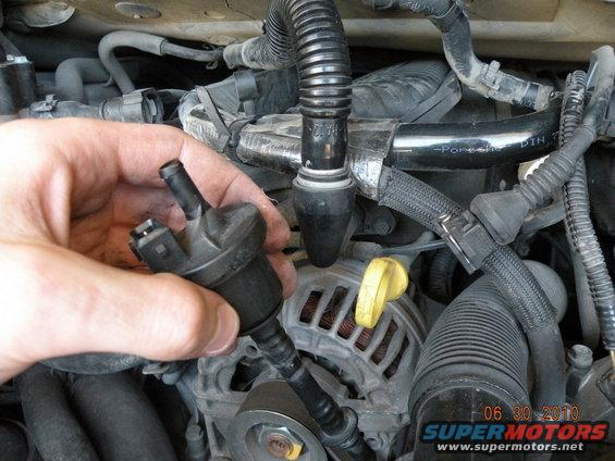 hand holding vacuum hose connector near engine components