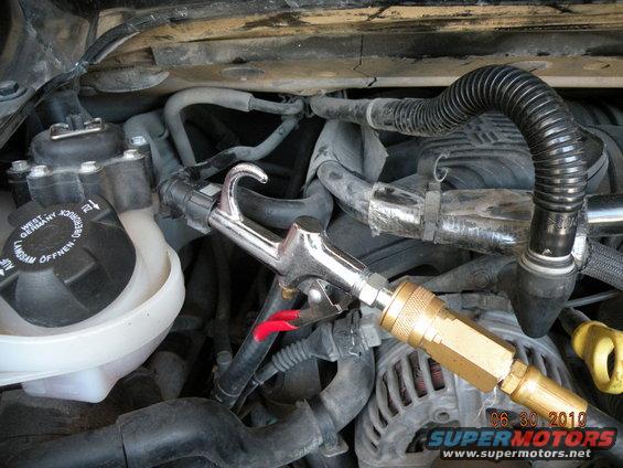 Engine bay with air duster nozzle attached to hoses and near a fluid reservoir