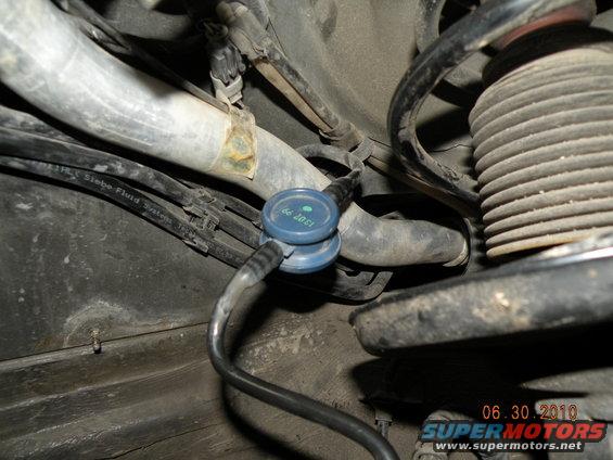 Close-up of automotive hoses and a blue valve, with suspension components visible