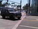 1986 Ford Bronco - A dark SUV drives through an intersection on a sunny day, with other vehicles visible in the background.