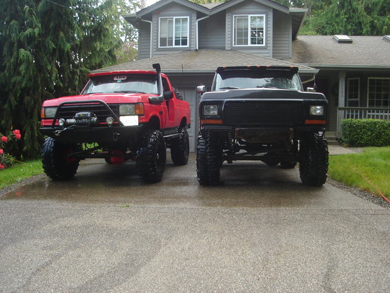 Two lifted trucks parked in front of a house, one red and one black
