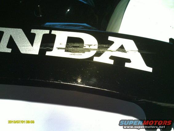 Black vehicle part with a scratched white Honda logo