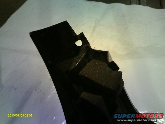 Black plastic automotive part with visible foam padding and mounting holes