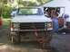 1989 Ford Bronco - Front view of a white pickup truck a bull bar and orange tie-down straps, with other vehicles and a garage in the background.