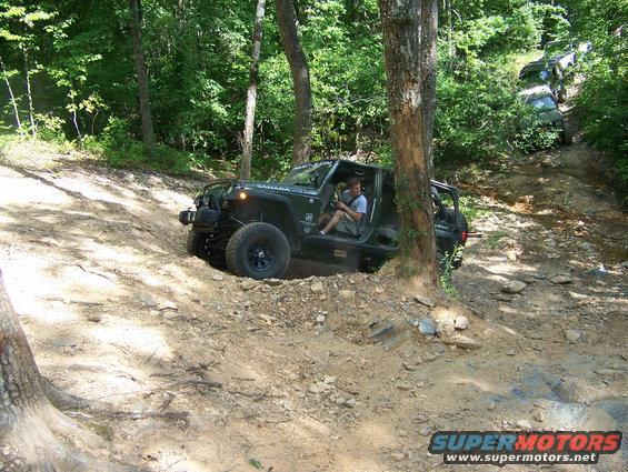 Black Jeep Wrangler Sahara climbing a rocky hill, driver visible