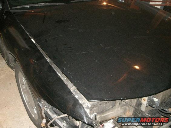 Black car hood and fender with visible scratches and damage to the front bumper area
