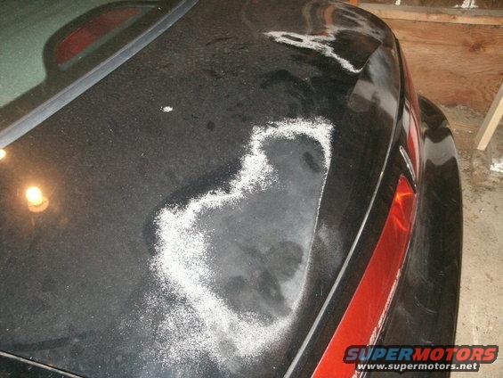 Black car trunk with peeling paint and white residue, showing a red taillight