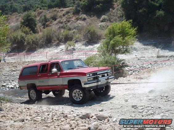 Red and silver SUV with aftermarket wheels driving off-road on a rocky path