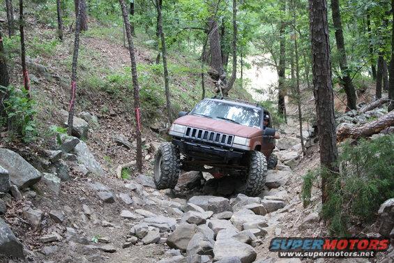 Brown Jeep Grand Cherokee navigating a rocky trail in the woods