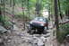 1984 Ford Bronco II - A Jeep Grand Cherokee tackles a challenging, rocky off-road course surrounded by trees.