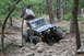 1984 Ford Bronco II - Two off-road vehicles tackle a challenging rocky path through a forest.