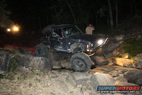 Black off-road vehicle with large tires navigating rocky terrain at night