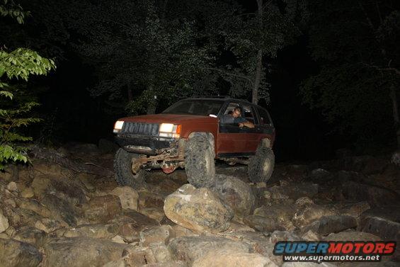 Orange Jeep Cherokee XJ driving over rocks at night