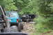 1984 Ford Bronco II - A convoy of off-road vehicles navigates a challenging, rocky trail surrounded by dense foliage.