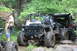 1984 Ford Bronco II - Two heavily modified off-road vehicles navigate a challenging rocky path in a wooded area.