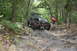 1984 Ford Bronco II - A heavily modified Jeep Wrangler TJ tackles a challenging rocky off-road course surrounded by dense forest.