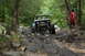 1984 Ford Bronco II - A modified off-road vehicle tackles a challenging rocky path through a wooded area.