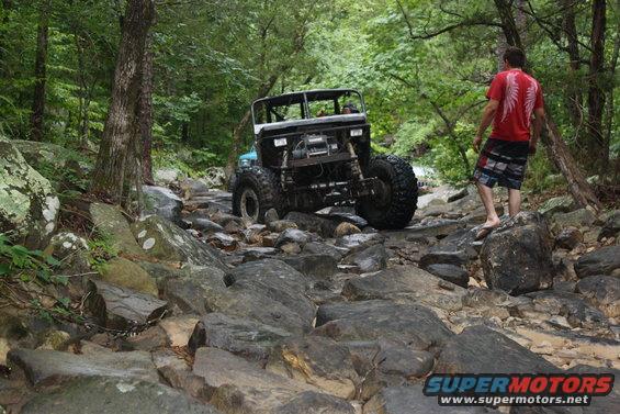 Modified off-road vehicle with large tires navigating a rocky stream bed