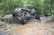 1984 Ford Bronco II - Modified Jeep navigates a challenging rocky trail with other off-road vehicles in the distance.