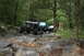 1984 Ford Bronco II - Multiple off-road vehicles traverse a challenging rocky path through a dense forest.