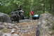 1984 Ford Bronco II - Two off-road vehicles traverse a challenging rocky path surrounded by dense forest.