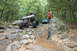 1984 Ford Bronco II - Off-road vehicles tackle a challenging rocky path through a wooded area, with one vehicle prominently featured on the left.