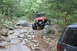1984 Ford Bronco II - Two off-road vehicles navigate a challenging rocky trail through a dense forest.