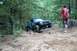 1984 Ford Bronco II - A person watches a teal Jeep Cherokee tackle a challenging off-road trail with large rocks and steep inclines.