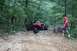 1984 Ford Bronco II - A red jeep navigates a rough, wooded trail with a person walking alongside.