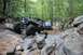 1984 Ford Bronco II - Off-road vehicles tackle a challenging rocky trail in a wooded area, with one vehicle in the lead and another following.