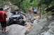 1984 Ford Bronco II - Multiple off-road vehicles traverse a challenging, rocky trail surrounded by dense foliage.