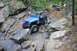 1984 Ford Bronco II - A blue Jeep Wrangler tackles a challenging rocky terrain, with other off-road vehicles visible further up the trail.