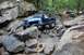 1984 Ford Bronco II - Several off-road vehicles traverse a challenging rocky terrain in a wooded area.