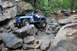 1984 Ford Bronco II - A blue Jeep Wrangler tackles a challenging rocky trail, with other off-road vehicles visible in the background.
