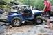 1984 Ford Bronco II - A blue Jeep navigates a challenging rocky trail, with several onlookers observing the off-road adventure.