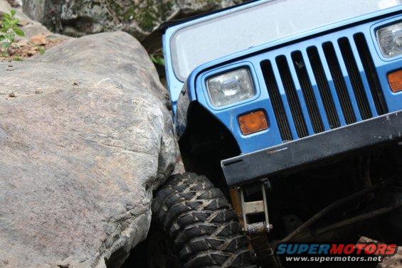 Blue Jeep Wrangler front grille and fender navigating a tight spot between large rocks