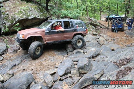 Modified Jeep Grand Cherokee climbing rocks, with other off-road vehicles in background