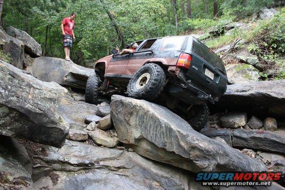 Jeep Grand Cherokee climbing over large rocks on a trail, driver visible inside