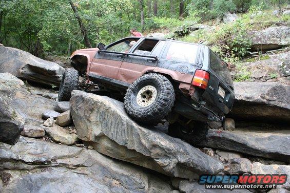 Brown and black Jeep Grand Cherokee off-roading over rocks, with large tires and lifted suspension
