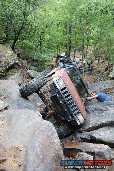 Brown Jeep Cherokee XJ tilted on rocks, driver's side front wheel off ground
