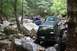 1984 Ford Bronco II - Several off-road vehicles navigate a challenging, rocky path through a dense forest.