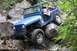 1984 Ford Bronco II - A blue Jeep Wrangler is shown off-roading over large rocks on a trail.