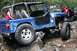 1984 Ford Bronco II - Two modified Jeeps navigate a rocky off-road trail in a wooded area.