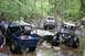 1984 Ford Bronco II - Multiple off-road vehicles traverse a challenging rocky stream in a wooded area.