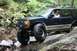 1984 Ford Bronco II - A dark blue and tan SUV navigates a rocky trail, its large tires gripping the terrain. The vehicle's body style suggests it is a 1991-1994…