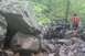 1984 Ford Bronco II - A Jeep navigates a challenging rocky terrain in a wooded area, with onlookers present.