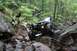 1984 Ford Bronco II - An off-road vehicle navigates a challenging rocky path through a dense forest.