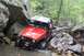 1984 Ford Bronco II - This red Jeep Wrangler is navigating a rocky stream bed in a wooded area.
