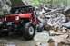 1984 Ford Bronco II - A heavily modified red off-road vehicle traverses a challenging rocky terrain with water flowing around its tires.